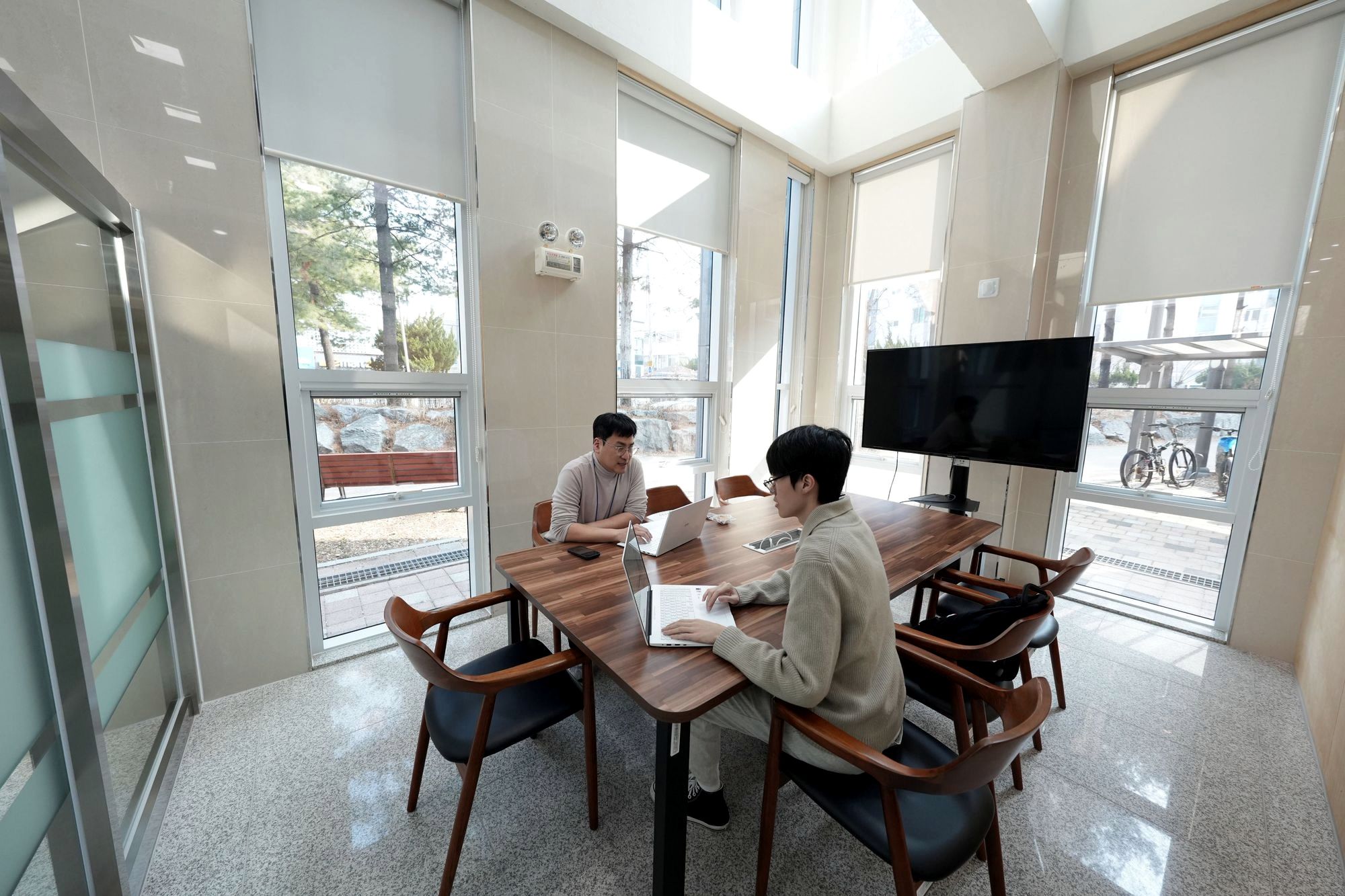 유리벽 회의실에서 투자심사역과 학생 대표가 마주 앉아 이야기하는 모습