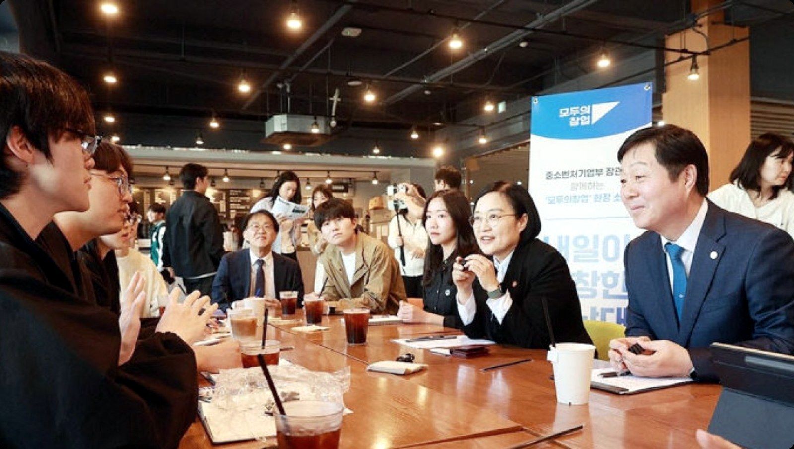 긴 테이블에 둘러앉아 장관과 이야기하는 학생 창업가들